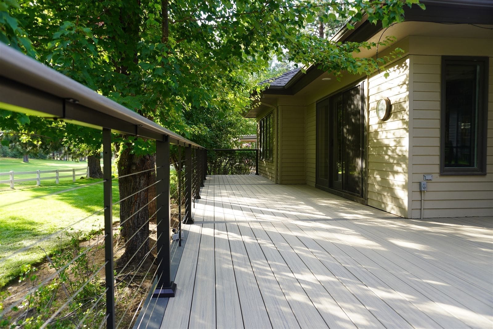 Covered composite deck with cable railing along a tree-shaded walkway